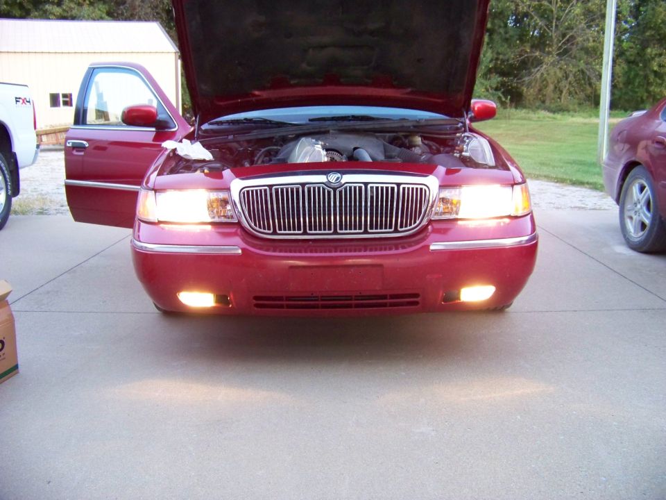 Red 1999 Mercury Grand Marquis front view, hood open, driver door ajar, headlights on