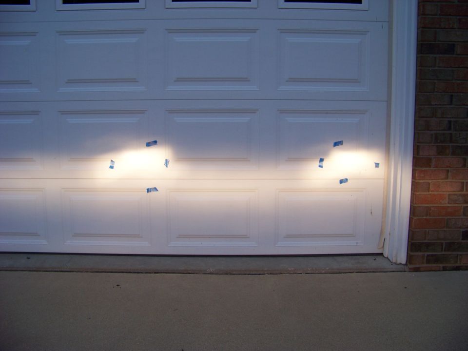Headlight beams projected onto a white garage door, taped for alignment
