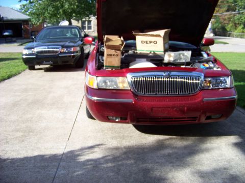 1999 Mercury Grand Marquis - Two Mercury Grand Marquis cars are parked outside. The red one has its hood open, revealing DEPO boxes.