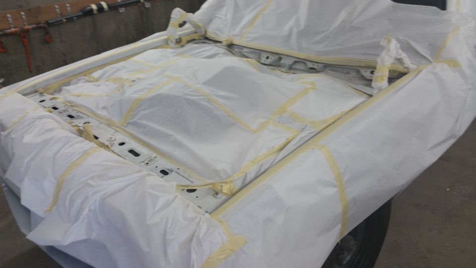 Vehicle chassis covered in masking paper and tape, showing exposed frame rails