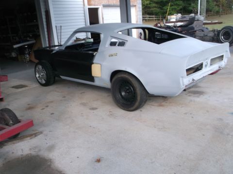 1967 Ford Mustang - A 1967 Ford Mustang is seen in a garage, partially prepped for paint with its body in primer and doors painted black.