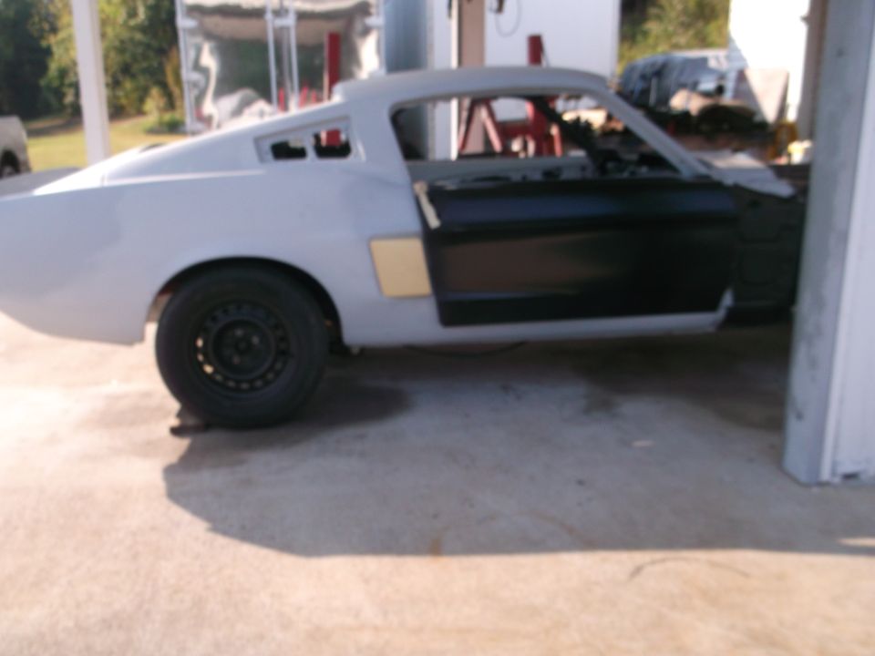 Side view of a 1967 Ford Mustang fastback in primer with doors open, undergoing restoration