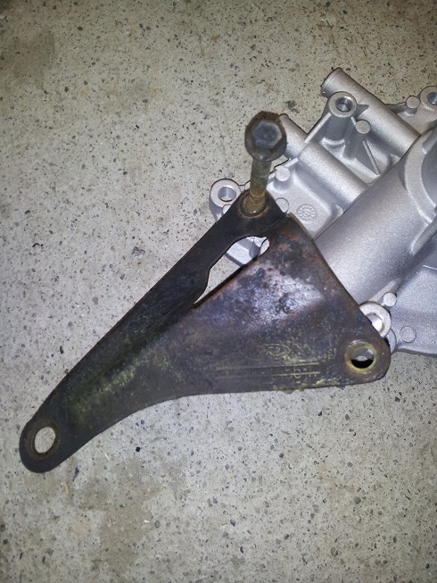 Rusty metal engine bracket with a bolt attached to a silver metal component, on a concrete surface