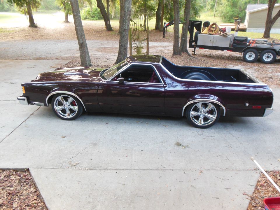 Lowered burgundy coupe utility on chrome multi-spoke wheels, driver-side profile on driveway