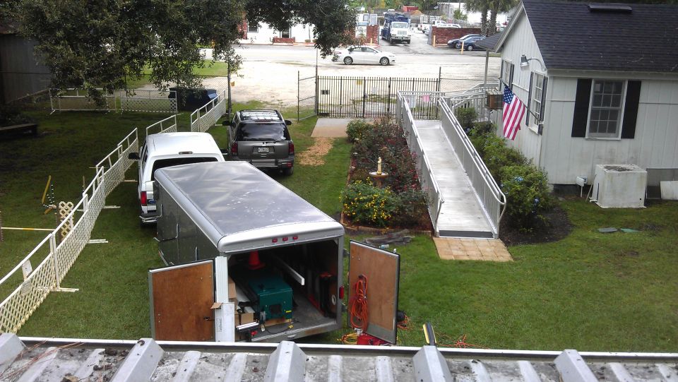 Open trailer parked next to an SUV in a yard with a ramp leading to a building
