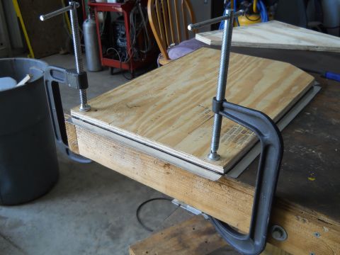 1992 Ford Bronco - Plywood is secured with C-clamps to a wooden workbench, likely for a woodworking project.