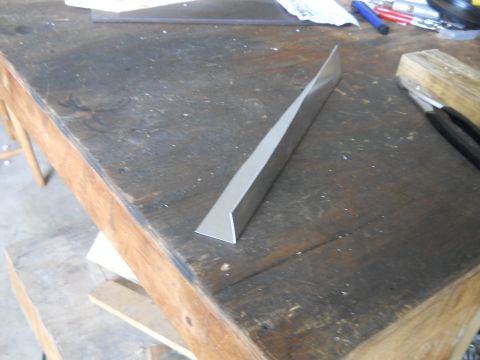1992 Ford Bronco - A metal trim piece rests on a weathered wooden workbench, with tools and papers in the background.
