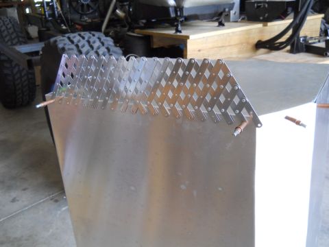 1992 Ford Bronco - Close-up of an aluminum panel diamond-shaped metal grating and copper fittings, with a tire and chassis visible in the background.