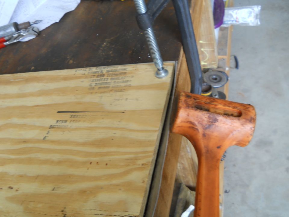 Workbench with a clamp holding plywood and a rubber mallet nearby. Text is visible on the plywood