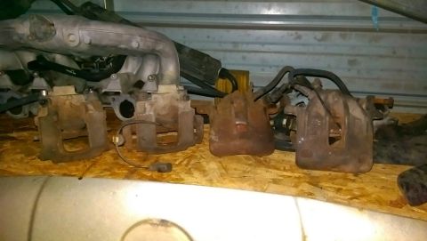 1989 BMW 3 Series - Collection of automotive parts, including brake calipers and an intake manifold, stored indoors.