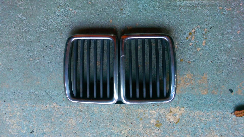 Pair of chrome-trimmed black BMW kidney grilles on a textured surface