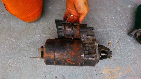 1989 BMW 3 Series - A used starter motor is held by a hand over a concrete surface.