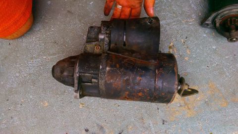 1989 BMW 3 Series - A rusty starter motor is shown on a concrete surface, with hands visible above it.