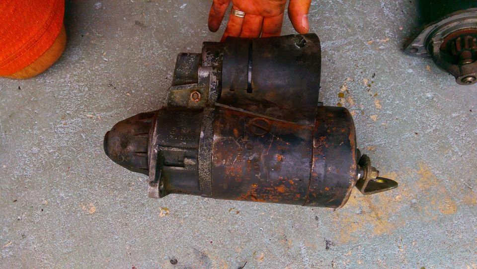 Old starter motor on concrete floor. Someone is holding it