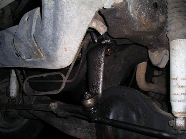 Underside view of a vehicle's steering linkage, tie rod, and suspension parts, with some grease and dirt visible
