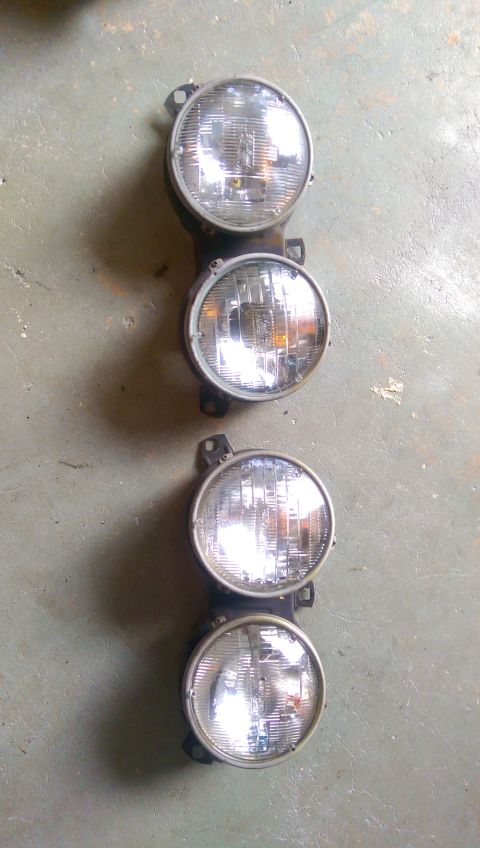 1989 BMW 3 Series - A set of four round headlights, likely for a classic car, are shown mounted on a bracket.