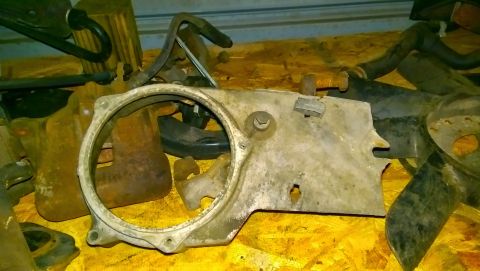 1989 BMW 3 Series - A collection of assorted engine parts, including a metal bracket with a large circular opening, are laid out on a wooden surface.