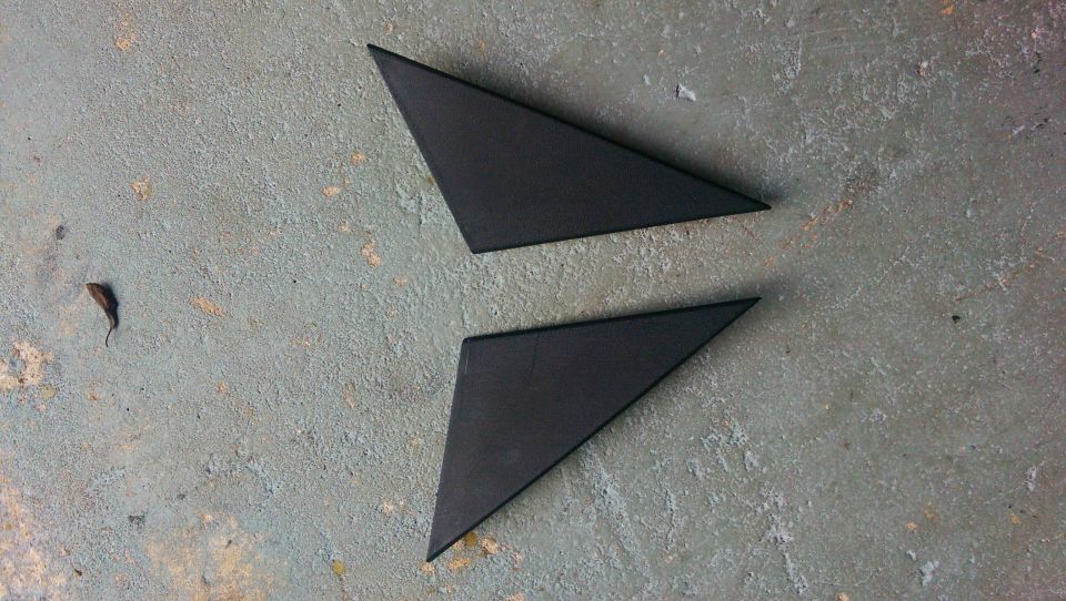Two black triangular trim pieces, possibly for car mirrors, on a concrete surface
