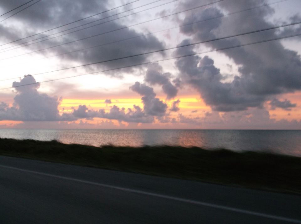 Ocean sunset with clouds and power lines over a road