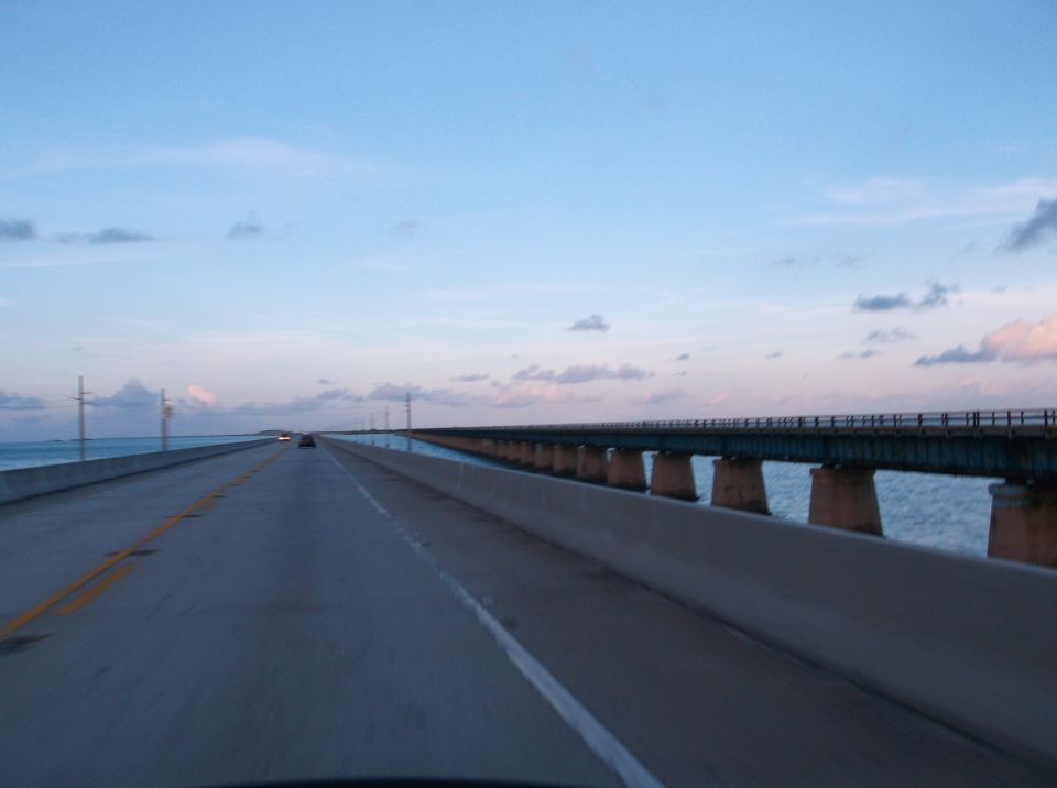 Highway bridge over the ocean at dusk with a few cars in the distance