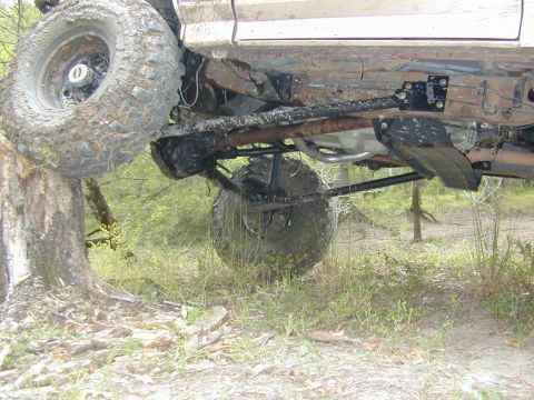 1996 Ford Bronco - The undercarriage of a vehicle is shown with one wheel elevated on a tree trunk in a wooded area.