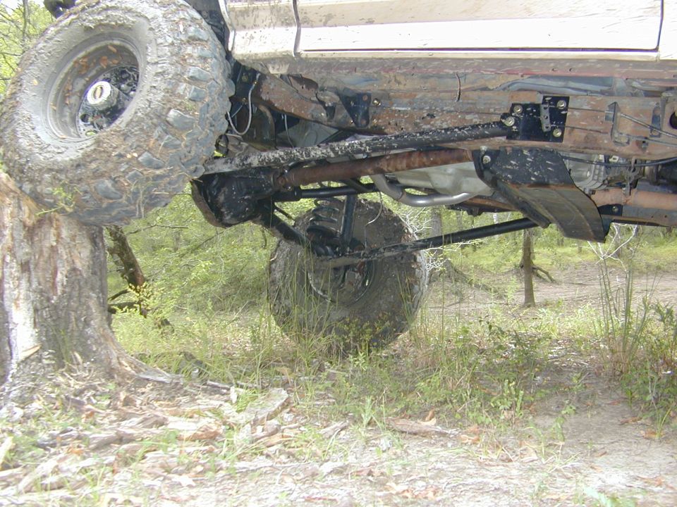 Undercarriage of lifted truck with muddy off-road tires, coil springs and rusty frame
