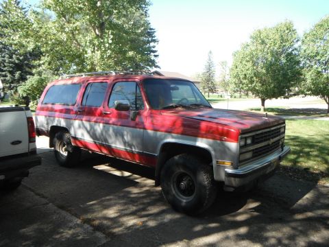 1990 Chevrolet Suburban - This 1990 Chevrolet Suburban features a two-tone red and silver paint scheme and is parked outdoors.