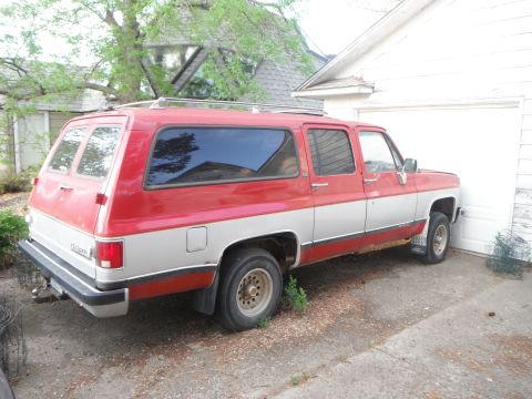 1990 Chevrolet Suburban - A two-tone red and silver Chevrolet Suburban is parked in a driveway next to a garage.
