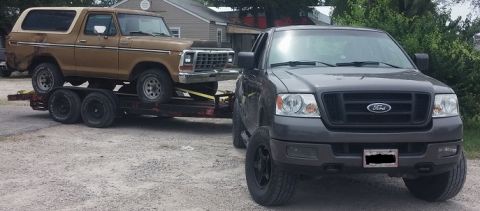 1979 Ford Bronco - A 1979 Ford Bronco is transported on a trailer, towed by a dark gray Ford pickup truck.