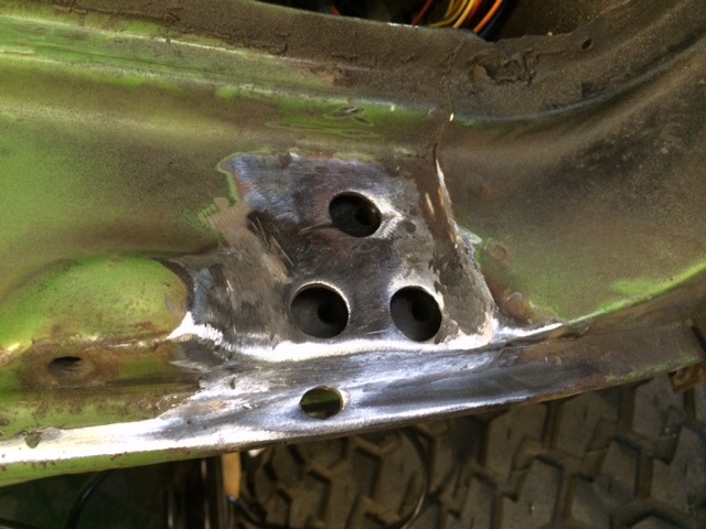 Green metal frame section with three drilled holes and evidence of welding