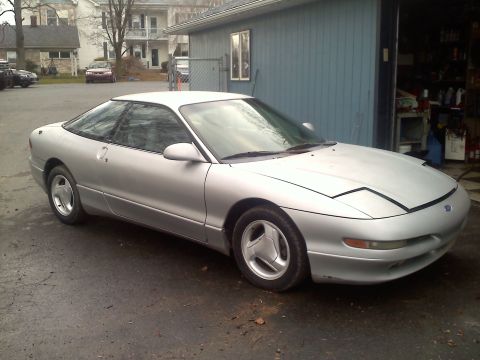 1993 Ford Probe - A silver 1993 Ford Probe GT is parked in front of a garage with houses in the background.