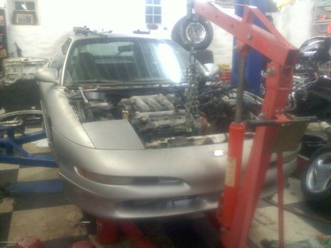 1993 Ford Probe - A silver 1993 Ford Probe is in a garage with its hood open as an engine hoist prepares to lift the engine.