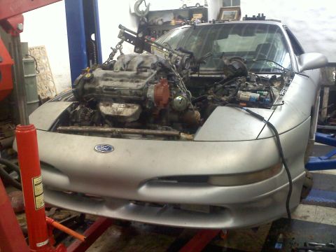 1993 Ford Probe - The engine bay of a silver Ford Probe is open as the engine is hoisted out of the vehicle.