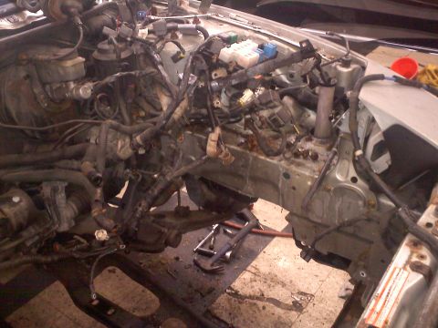 1993 Ford Probe - Engine bay disassembled, showing complex wiring and internal components. Tools are visible on the ground.