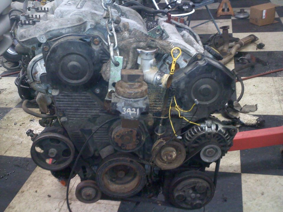 Engine block with timing covers, pulleys, alternator, and yellow dipstick. Part number 3421 visible