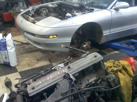 1993 Ford Probe - A silver car, possibly a Ford Probe, is shown with its hood open and engine removed, in what appears to be a repair shop.