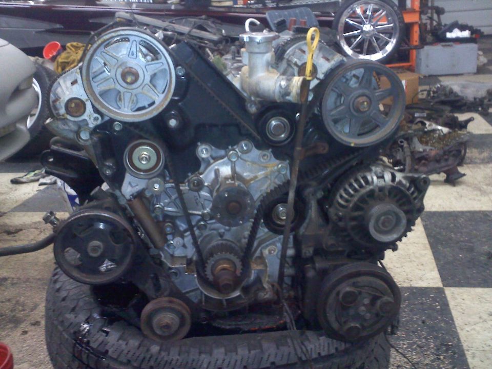Engine assembly with belts, pulleys, and alternator. Water pump visible at top center. Supermotors.net logo at bottom right