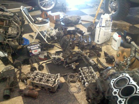 1993 Ford Probe - Scattered engine components and a car battery are visible on a checkered garage floor, with a dog observing from the side.
