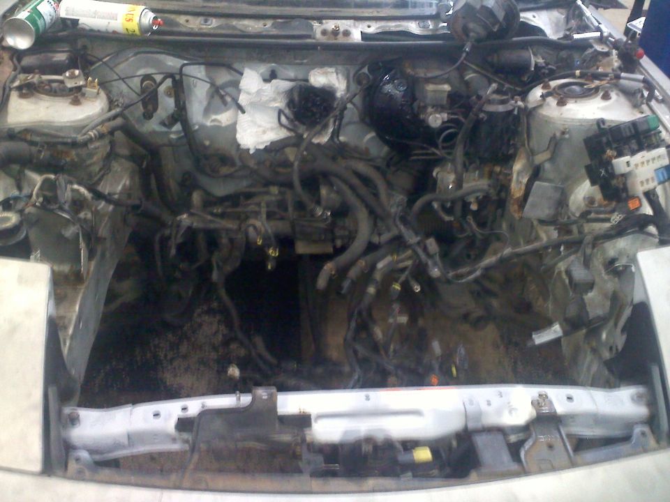 Engine bay with wiring and hoses disconnected, car disassembled