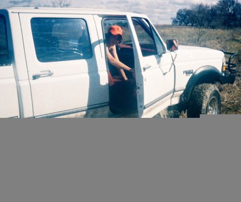 1991 Ford Bronco - A person is getting into a white crew cab pickup truck in a grassy, outdoor area.