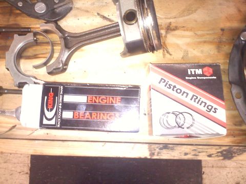 1993 Ford Probe - Engine parts laid out on a workbench, including a piston, connecting rod, and new engine bearings and piston rings.