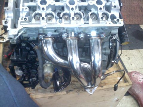 1993 Ford Probe - Engine block with a shiny chrome exhaust manifold and an attached sensor, resting on a wooden crate.