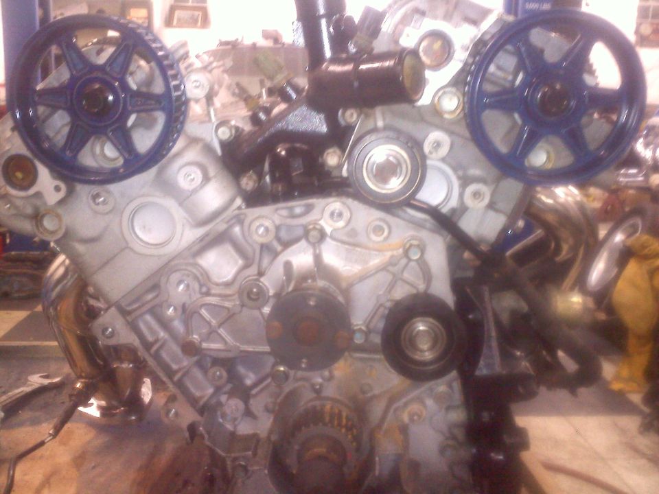 Engine block with blue timing gears and various pulleys and belts visible