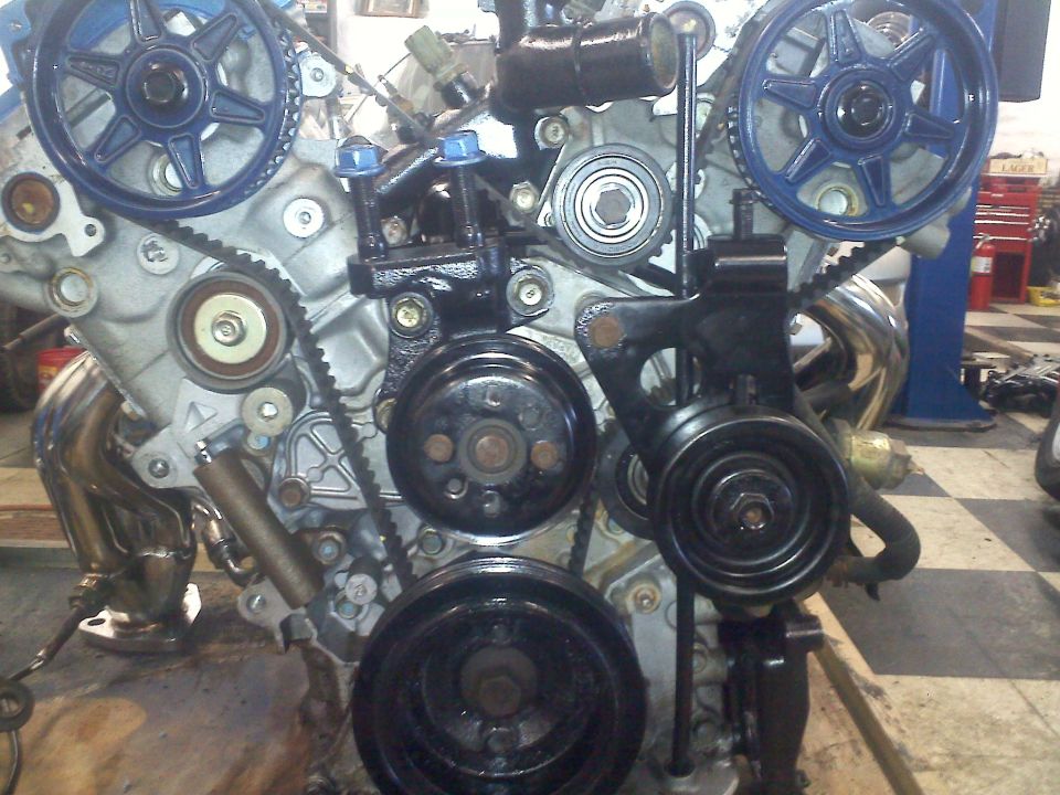 Engine with blue-painted pulleys and black accessories, showing timing belt and exhaust manifold