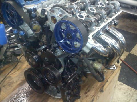 1993 Ford Probe - Close-up view of an engine assembly blue timing belt pulleys and a chrome exhaust manifold.
