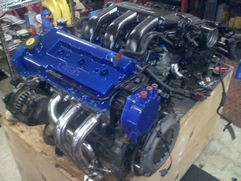 1993 Ford Probe - Engine assembly with blue Ford valve covers and chrome exhaust headers is displayed on a wooden crate.
