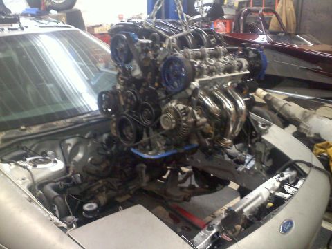 1993 Ford Probe - Mechanic is removing the engine from a car in a workshop. Another vehicle is parked nearby.