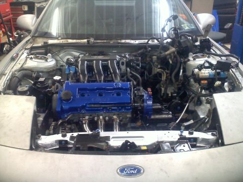 1993 Ford Probe - The engine bay of a silver Ford Probe is visible, with the engine partially removed and a blue engine block in place.