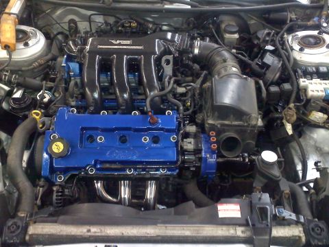 1993 Ford Probe - Engine bay a V6 engine with custom blue valve covers and aftermarket exhaust headers.