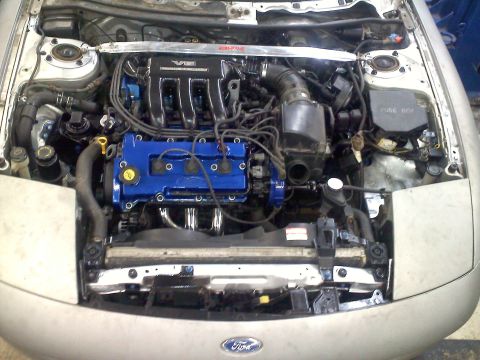 1993 Ford Probe - The V6 engine bay of a Ford Probe, blue painted valve covers and chrome exhaust manifolds.